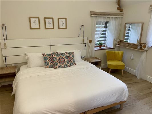 King size bed with white bed linen. A small yellow chair is in the right corner under the bedroom window.